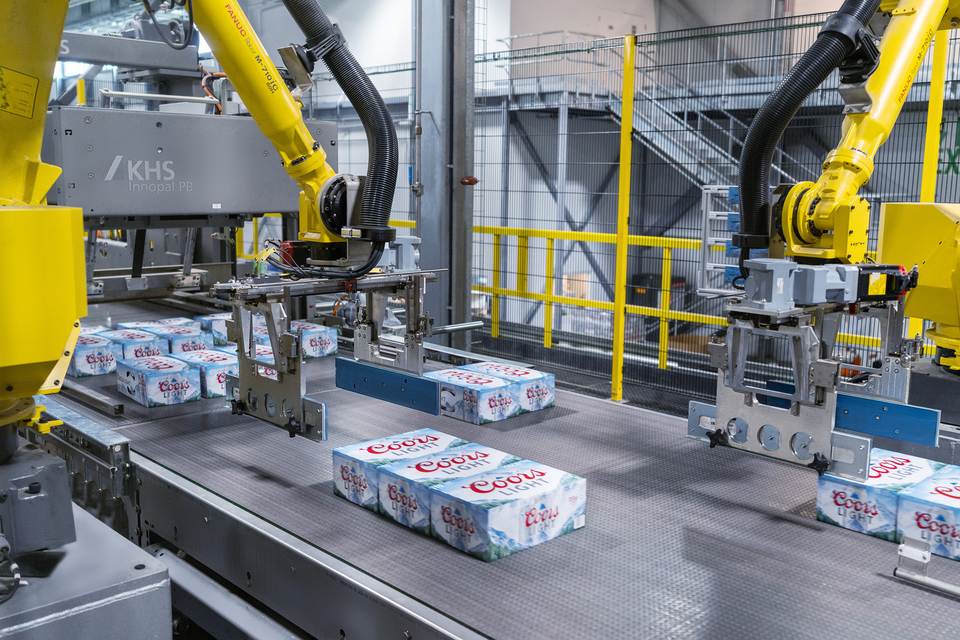 Wrap-around can packs are grouped into layers by gripping robots prior to being palletized.