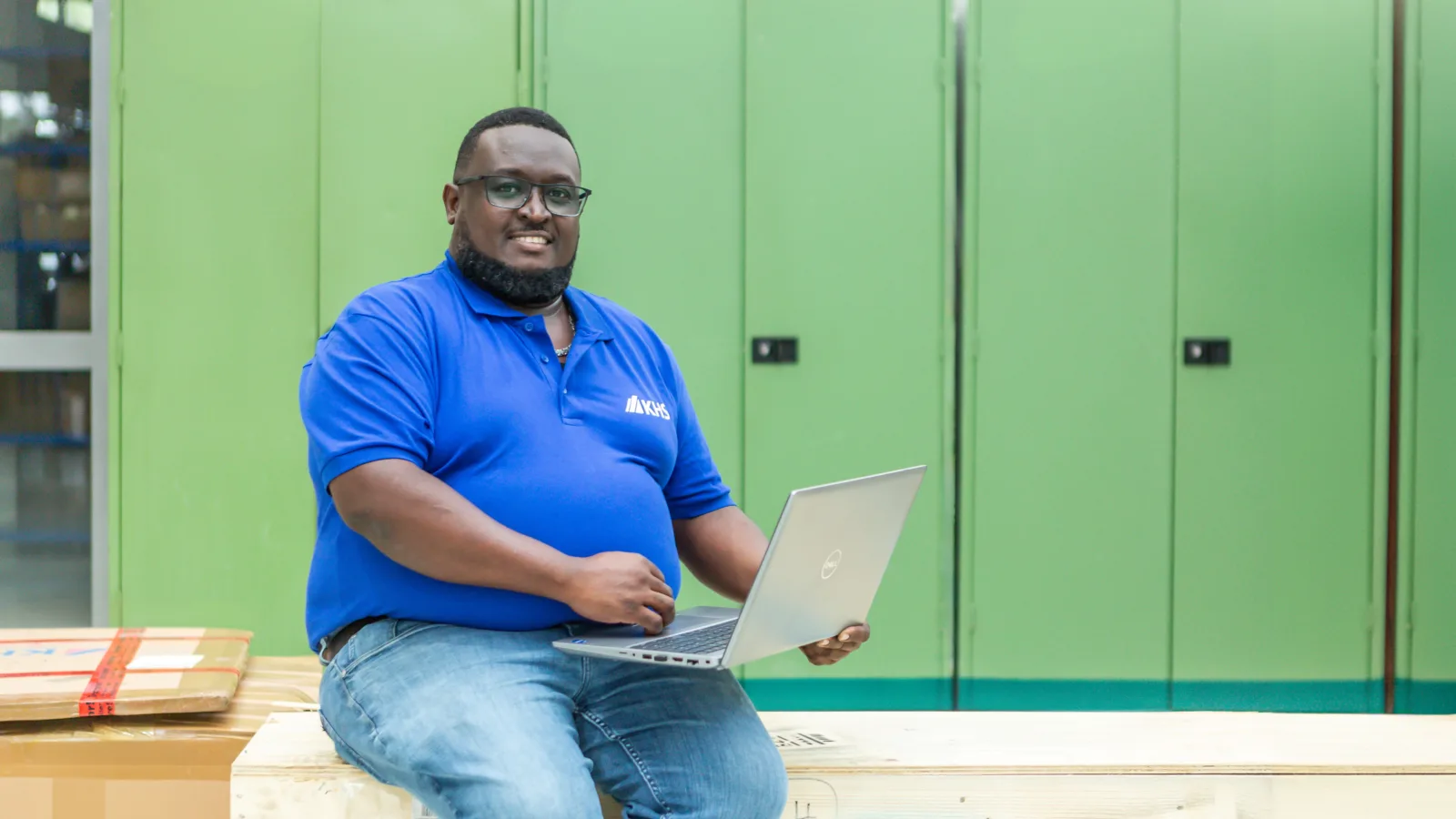 Matthew Ndolo sits on packages in front of a green metal cupboard