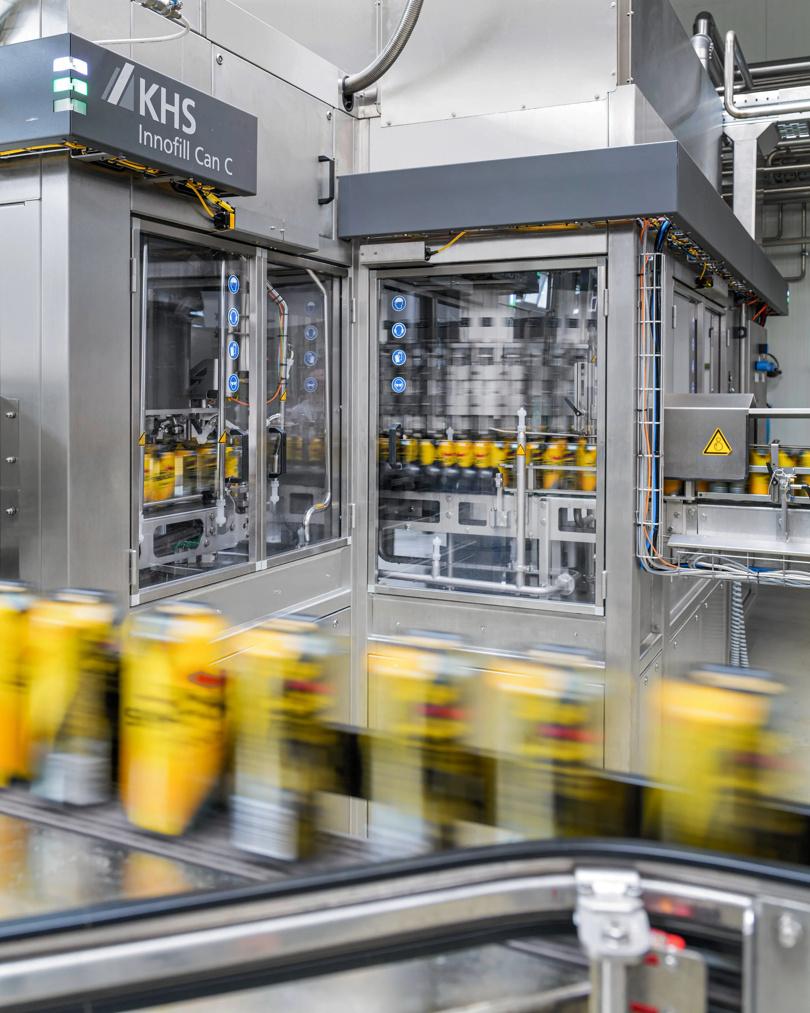 En primer plano se pueden ver latas de bebidas borrosas por el movimiento. Al fondo se puede ver la máquina llenadora de latas KHS Innofill Can C.