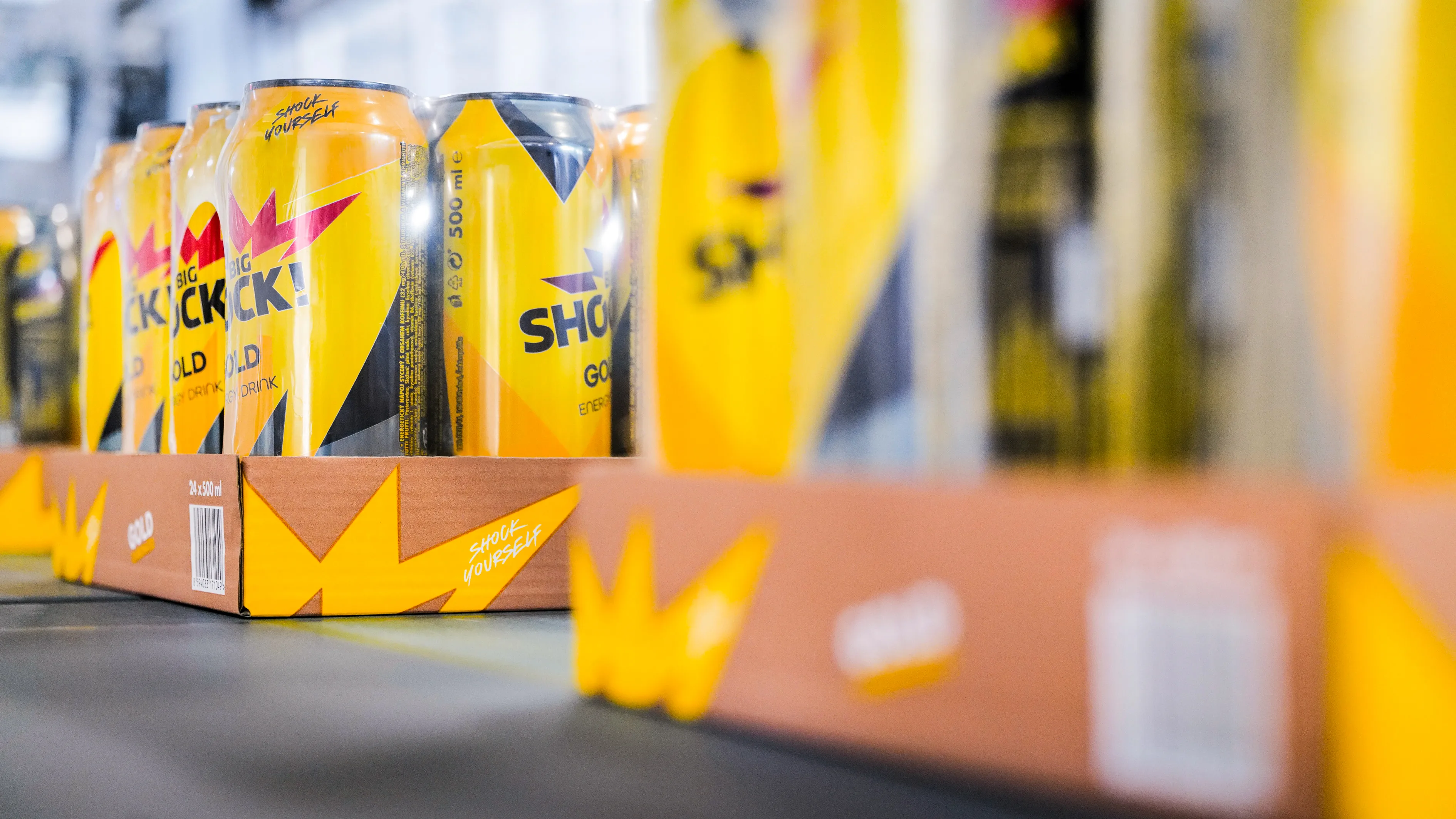 Yellow and black beverage cans are already packed in half-height boxes on a conveyor belt