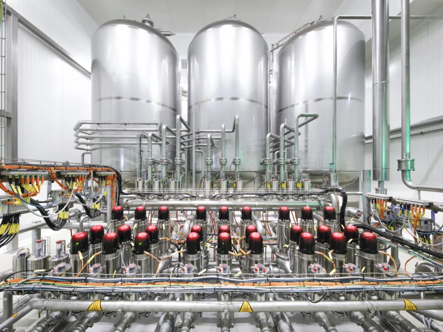 The picture shows 3 beer storage tanks in the background with a fully automatic valve node in the foreground.