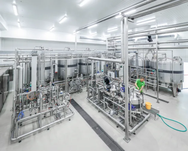 You can see the multifunctional syrup room, with large mixing tanks in the background. In the foreground is an employee working on the system.