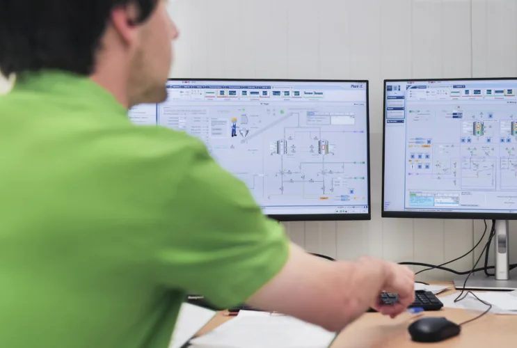 A man in a green T-shirt sits in front of two monitors that control the semi-automatic syrup room.