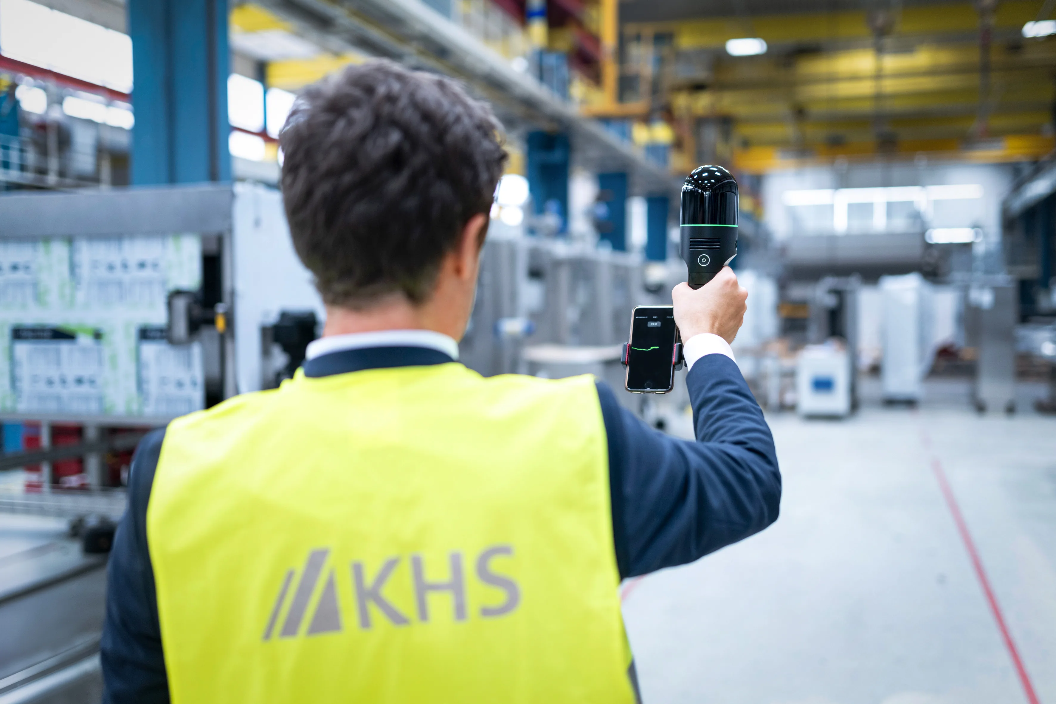 Mann mit KHS Schutzweste hält den Laserscanner in der Hand, während er sich durch eine Halle bewegt