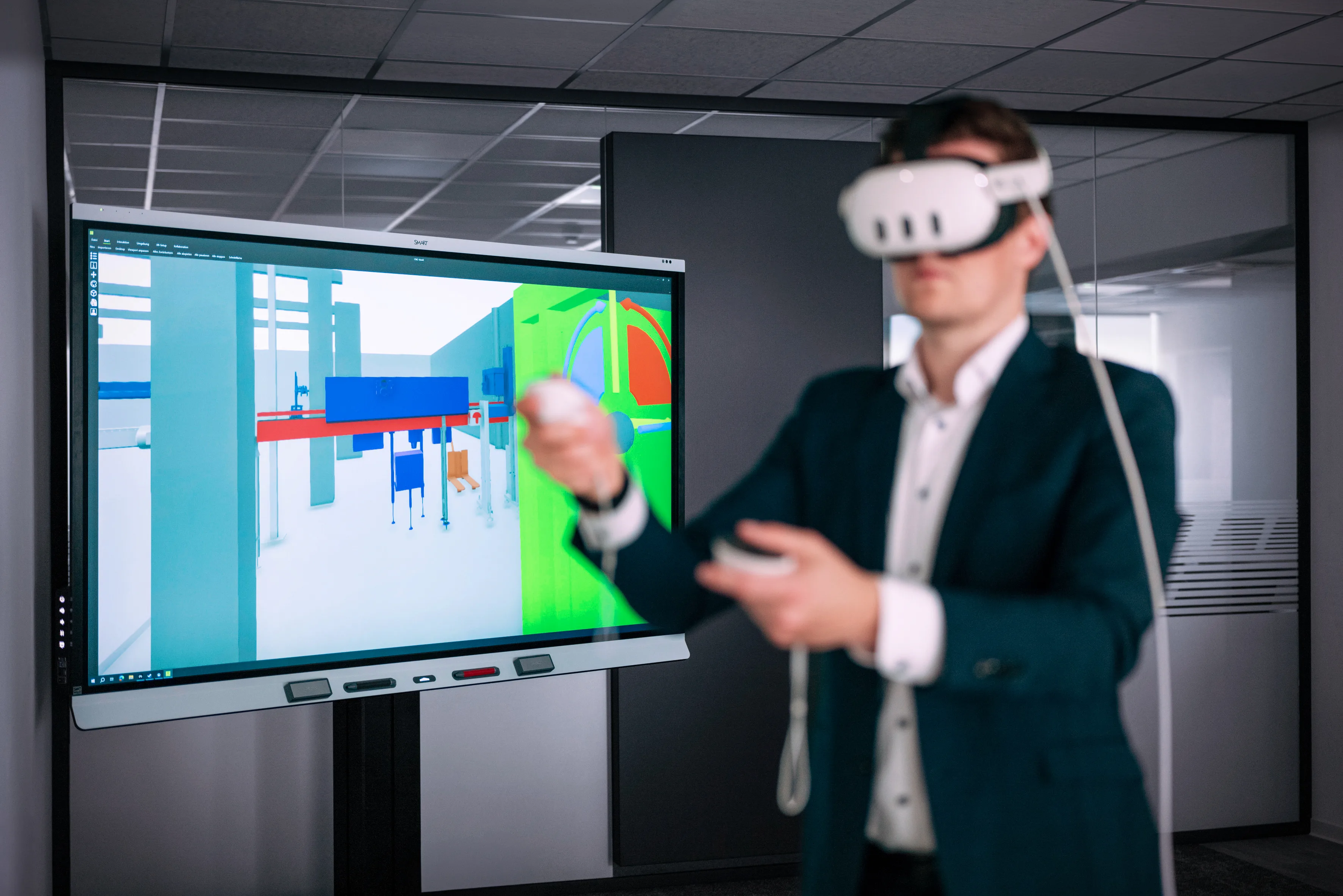 A man wearing a virtual reality headset stands in front of a large screen showing digital content.