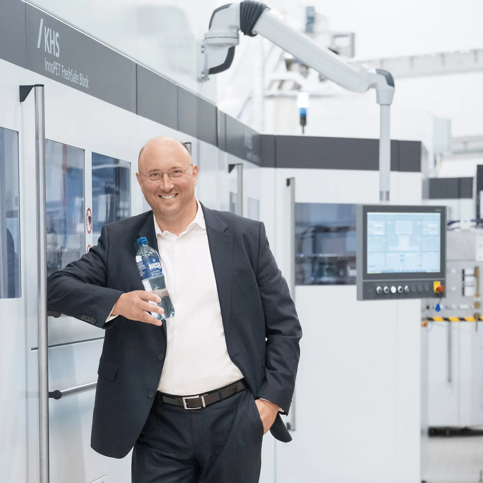 Mr. Rodekohr in a suit, leaning against a machine, holds a bottle of water in his hand
